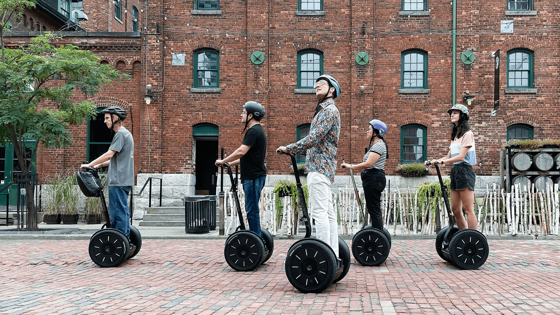 Group of Segway tour participants exploring historic red brick Victorian buildings on cobblestone streets during Distillery District Segway Spin tour in Toronto